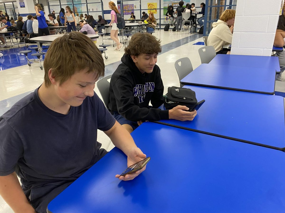 Students, now unable to use phones elsewhere, sit together on their phones in the cafeteria.