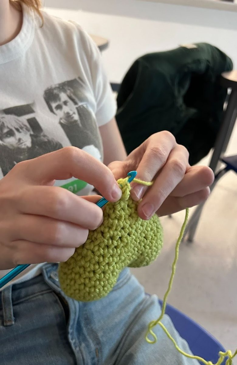 A student crocheting a green heart at Crochet Club. 